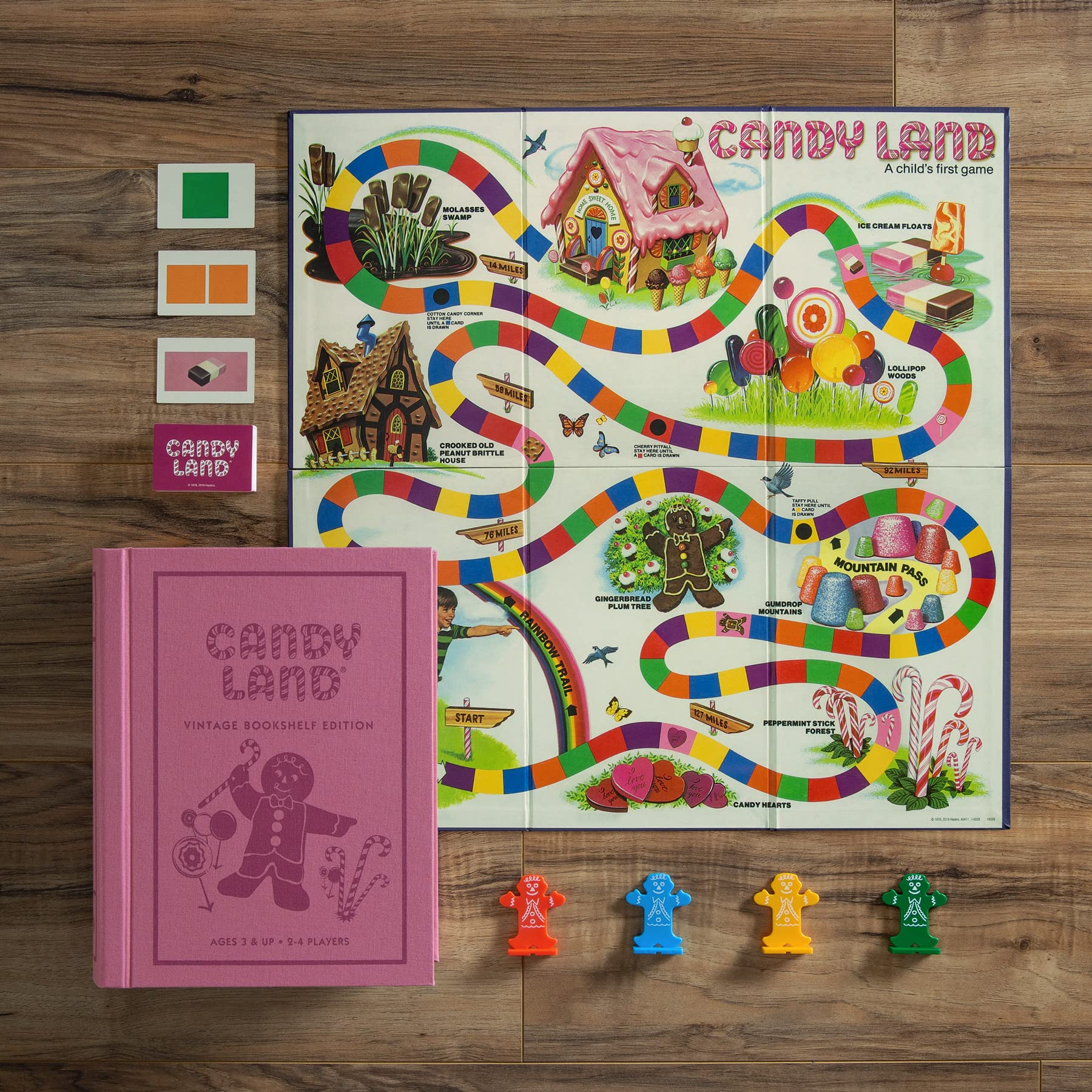 Candy Land board game set with colorful board, pink book, and game pieces on a wooden surface.