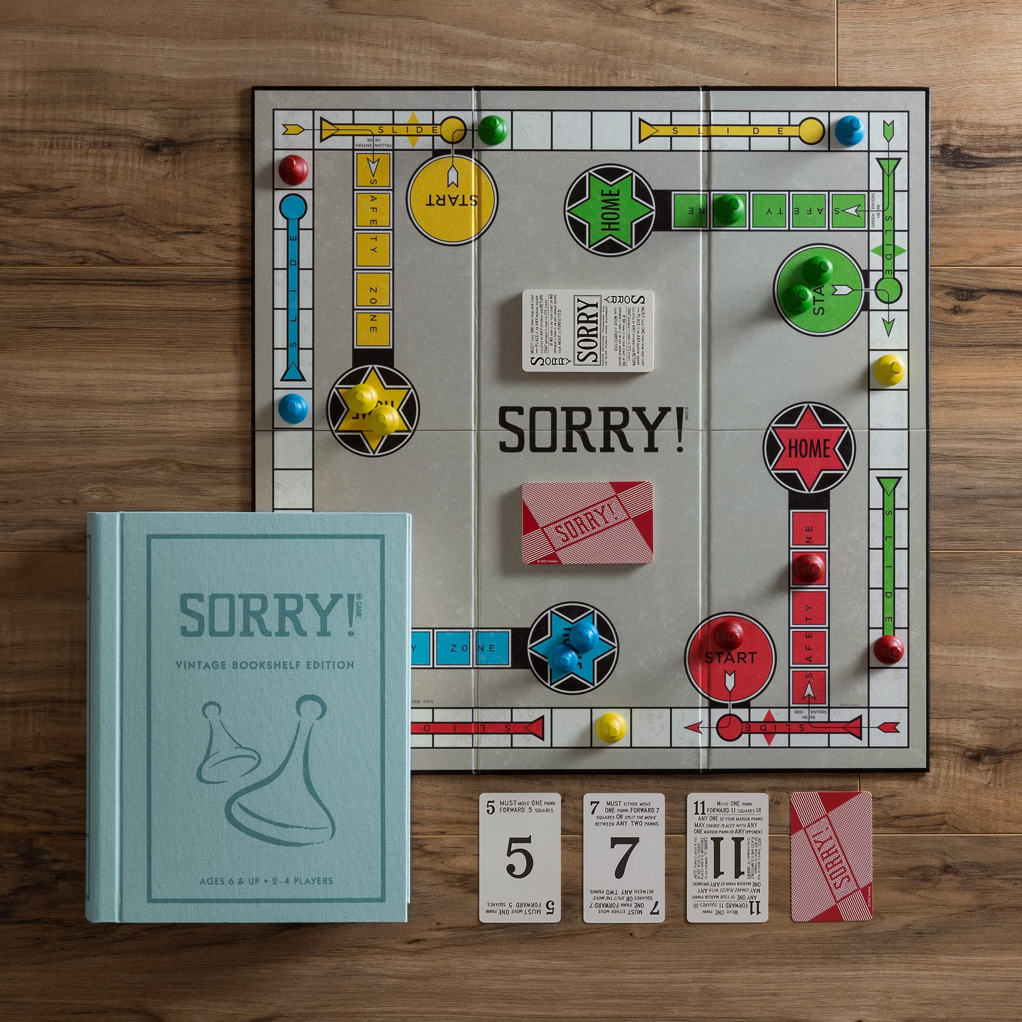Sorry! board game set on a wooden surface with the book 'Sorry! Vintage Bookshelf Edition' and game pieces.